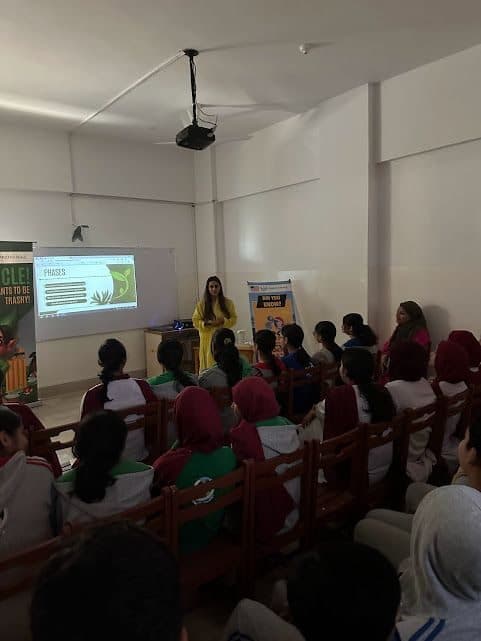 Lalain at the front of a classroom beside a Recycle banner and a slide
