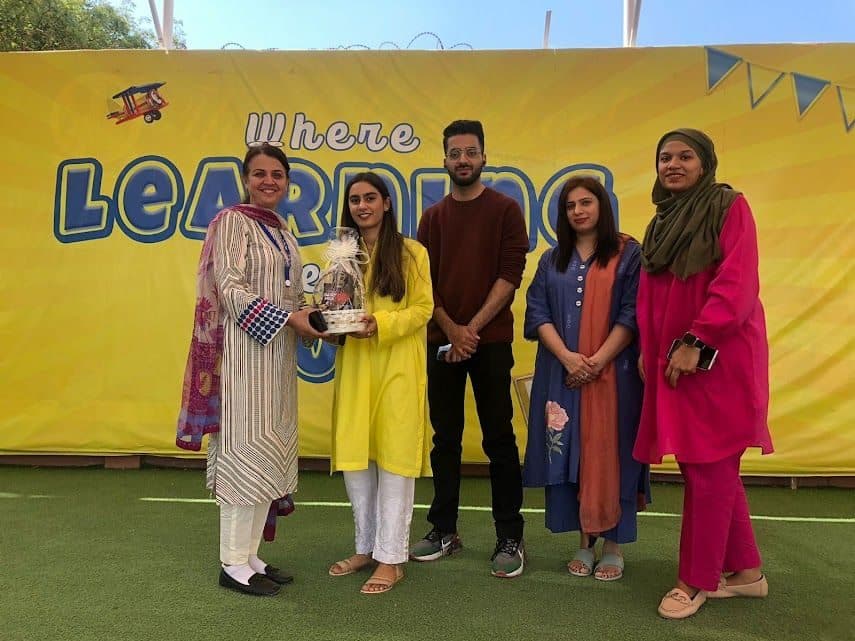 Lalain in yellow receiving a gift from school staff in front of a Where Learning banner