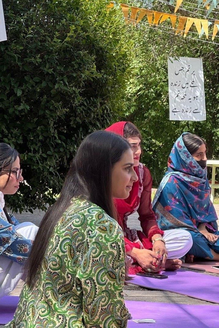 Lalain in a green paisley kurta, listening in a discussion circle under bunting at the FIERCE Institute
