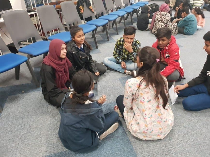 Lalain sitting on the floor in a circle with young campers, talking through their ideas