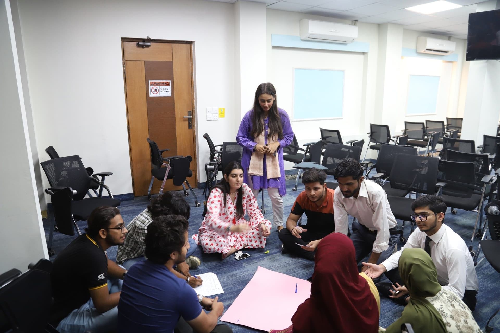Lalain standing over a group of young people working on chart paper on the floor